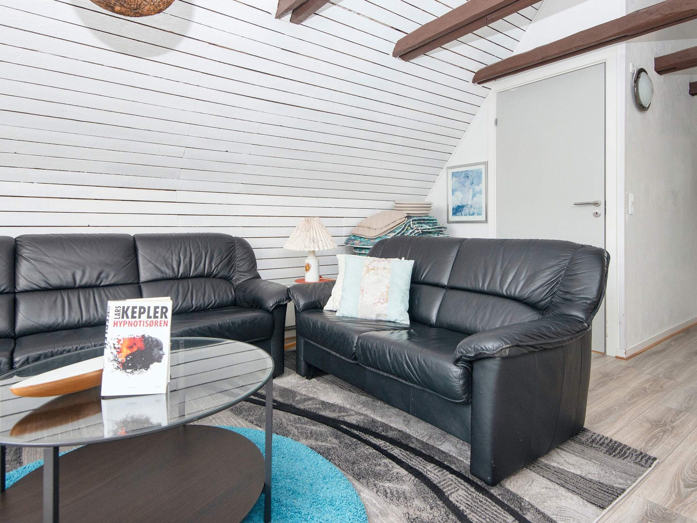 A modern living room with two black leather sofas, a glass coffee table, and a blue rug.