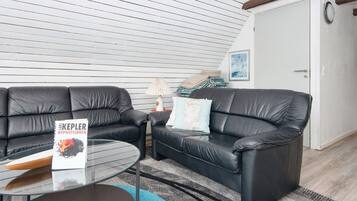 A modern living room with two black leather sofas, a glass coffee table, and a blue rug.