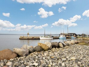 Una costa rocosa con barcos amarrados en un muelle, un faro y una construcción con techo de paja.