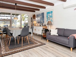 Una sala moderna con un sofá gris, una mesa de comedor con mantel a cuadros y un ventanal grande.