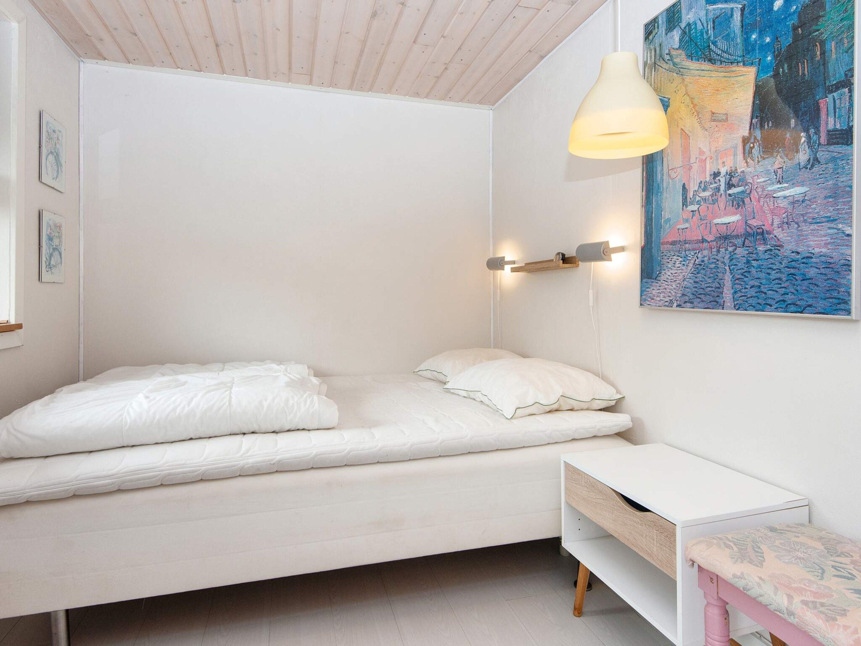 A minimalist bedroom with a bed, bedside table, and a wall-mounted light fixture.