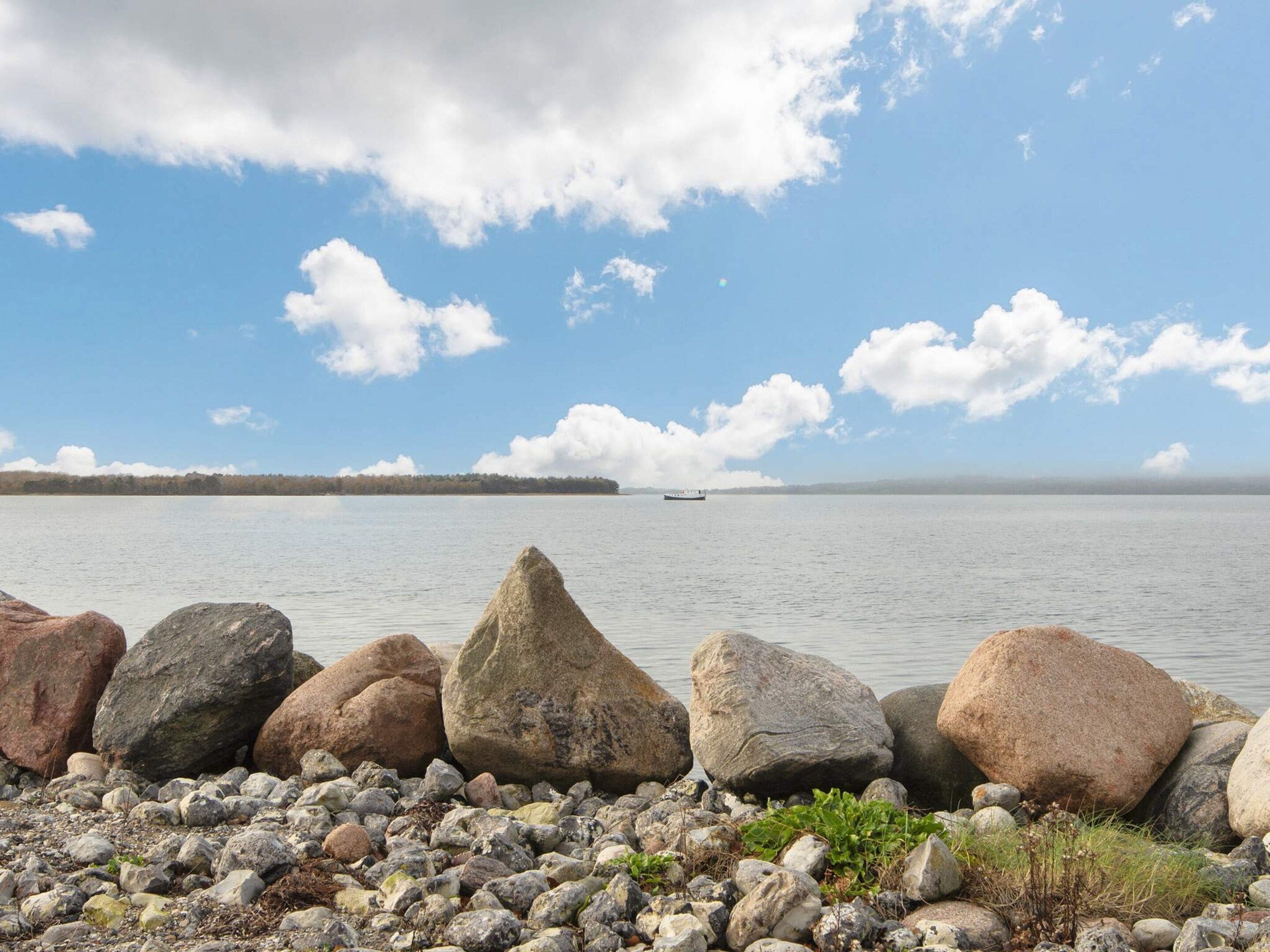 A rocky shoreline with a calm body of water, a distant landmass, and a clear sky.