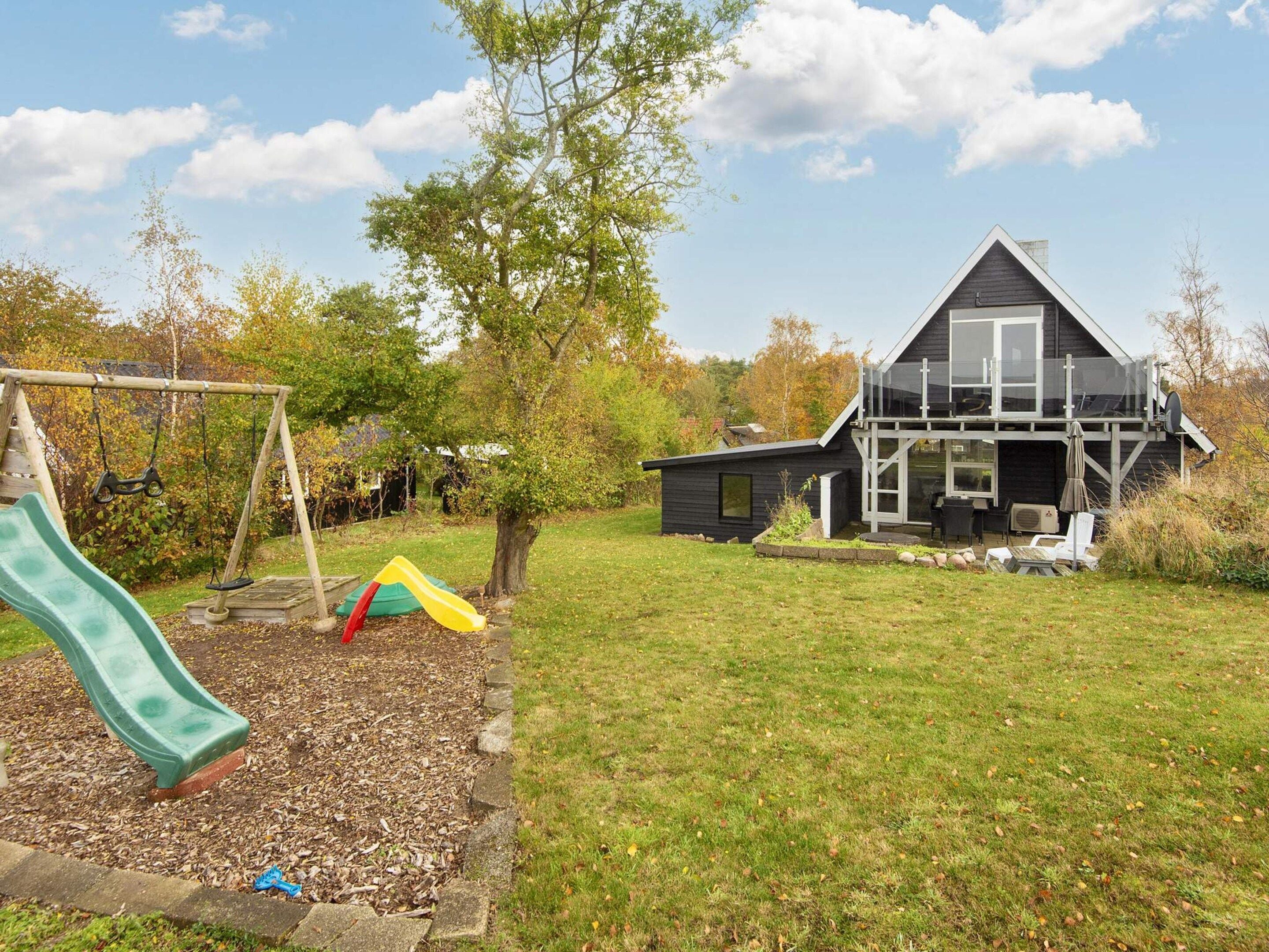 A residential property with a play area including a slide and swings, a modern house with a large window, and a clear sky.