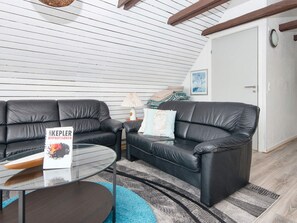 A modern living room with two black leather sofas, a glass coffee table, and a blue rug.