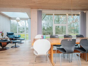 A modern dining area with a wooden table and chairs, a large window with curtains, and a seating area with a leather chair and a small table. - 8 Person Holiday Home in Blavand (Blavand)