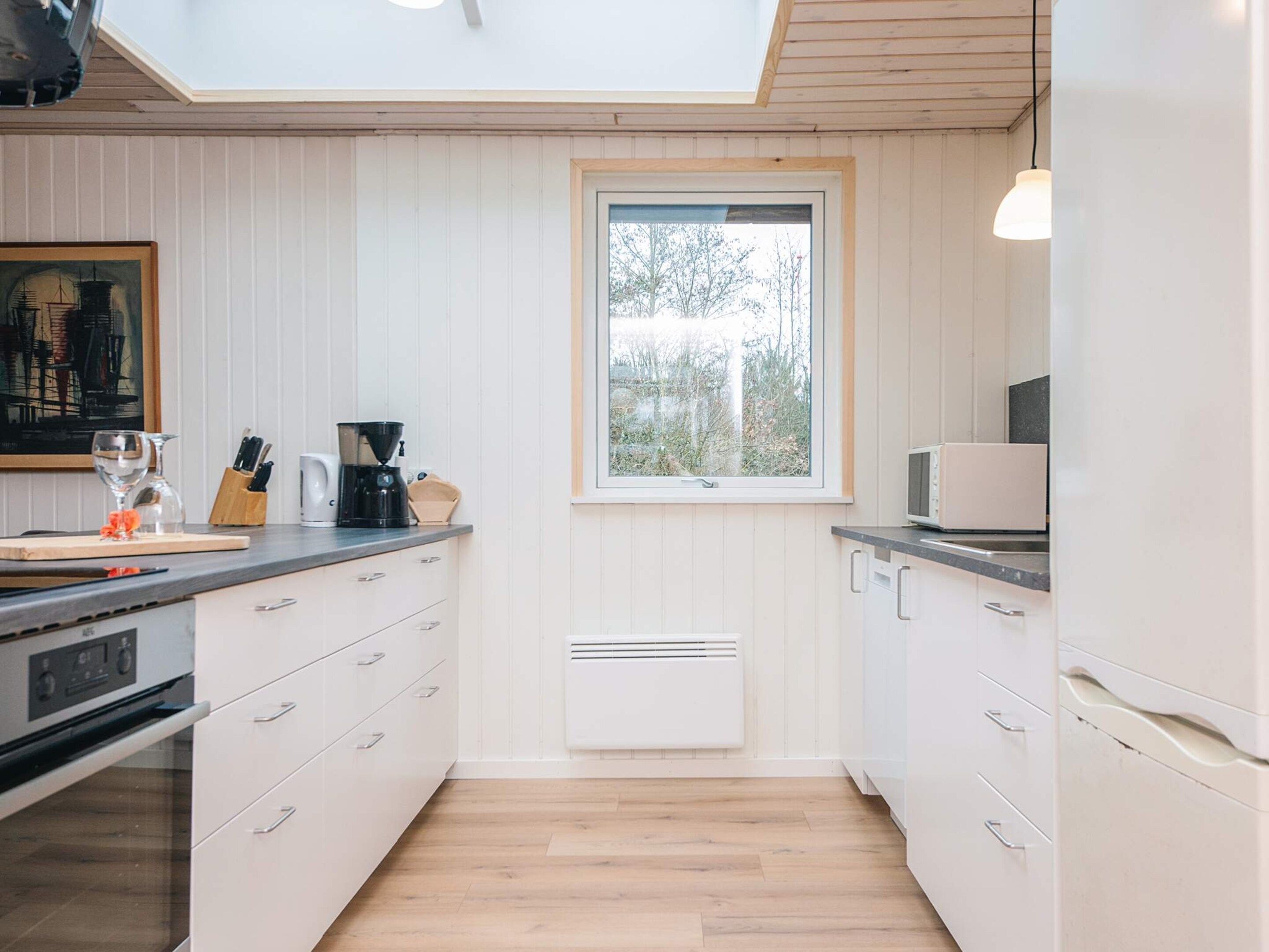 Una cucina moderna con mobili bianchi, forno integrato, macchina da caffè e una finestra che lascia entrare luce naturale.