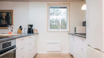 Una cucina moderna con mobili bianchi, forno integrato, macchina da caffè e una finestra che lascia entrare luce naturale.