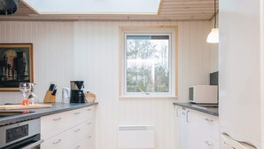 A modern kitchen with white cabinetry, a built-in oven, a coffee maker, and a window with a view of trees. - 8 Person Holiday Home in Blavand (Blavand)