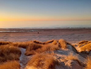 A beach with dunes in the foreground and a calm sea in the background. - 8 Person Holiday Home in Blavand (Blavand)