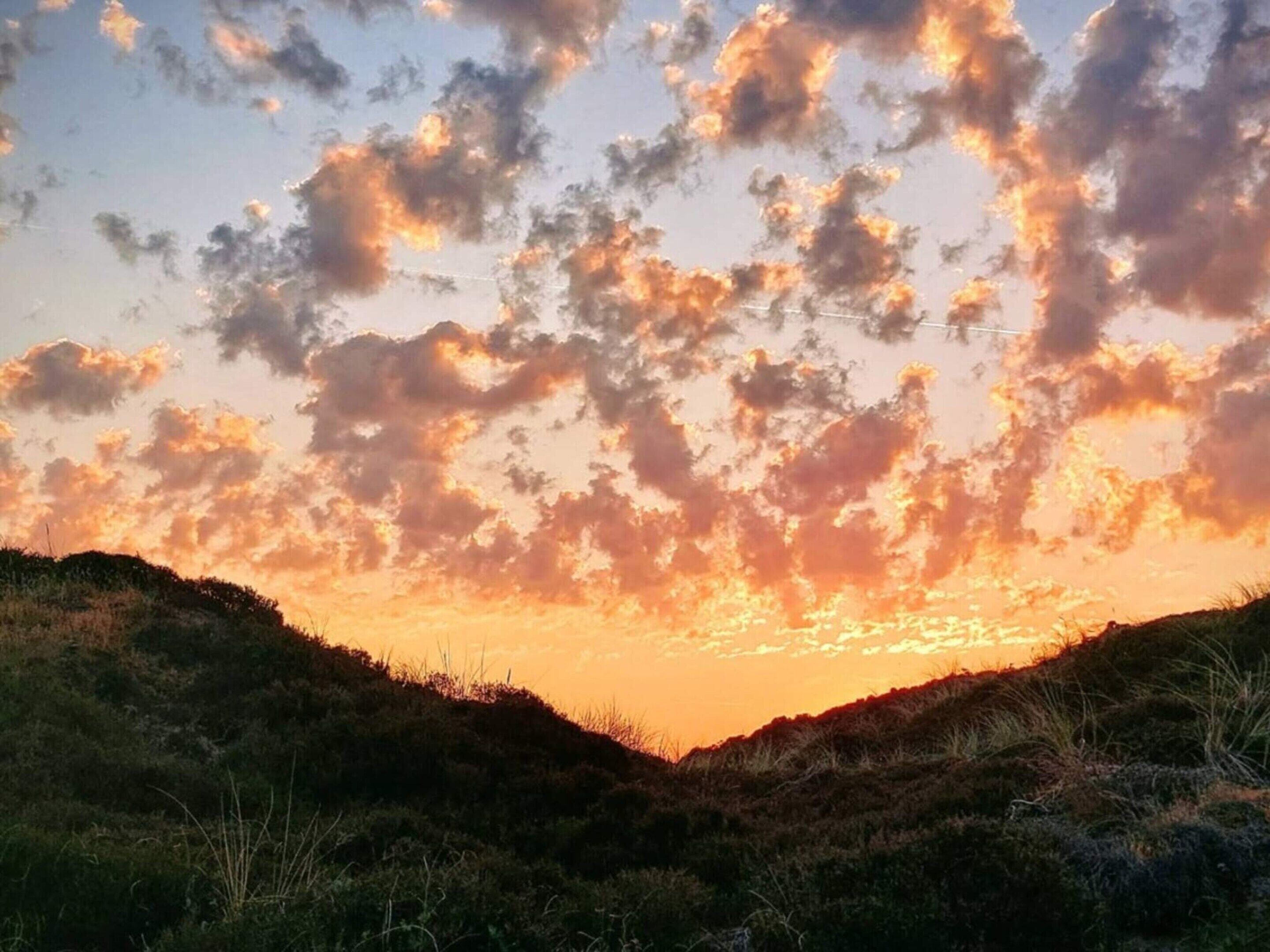 Un atardecer sobre un paisaje montañoso con nubes dispersas.