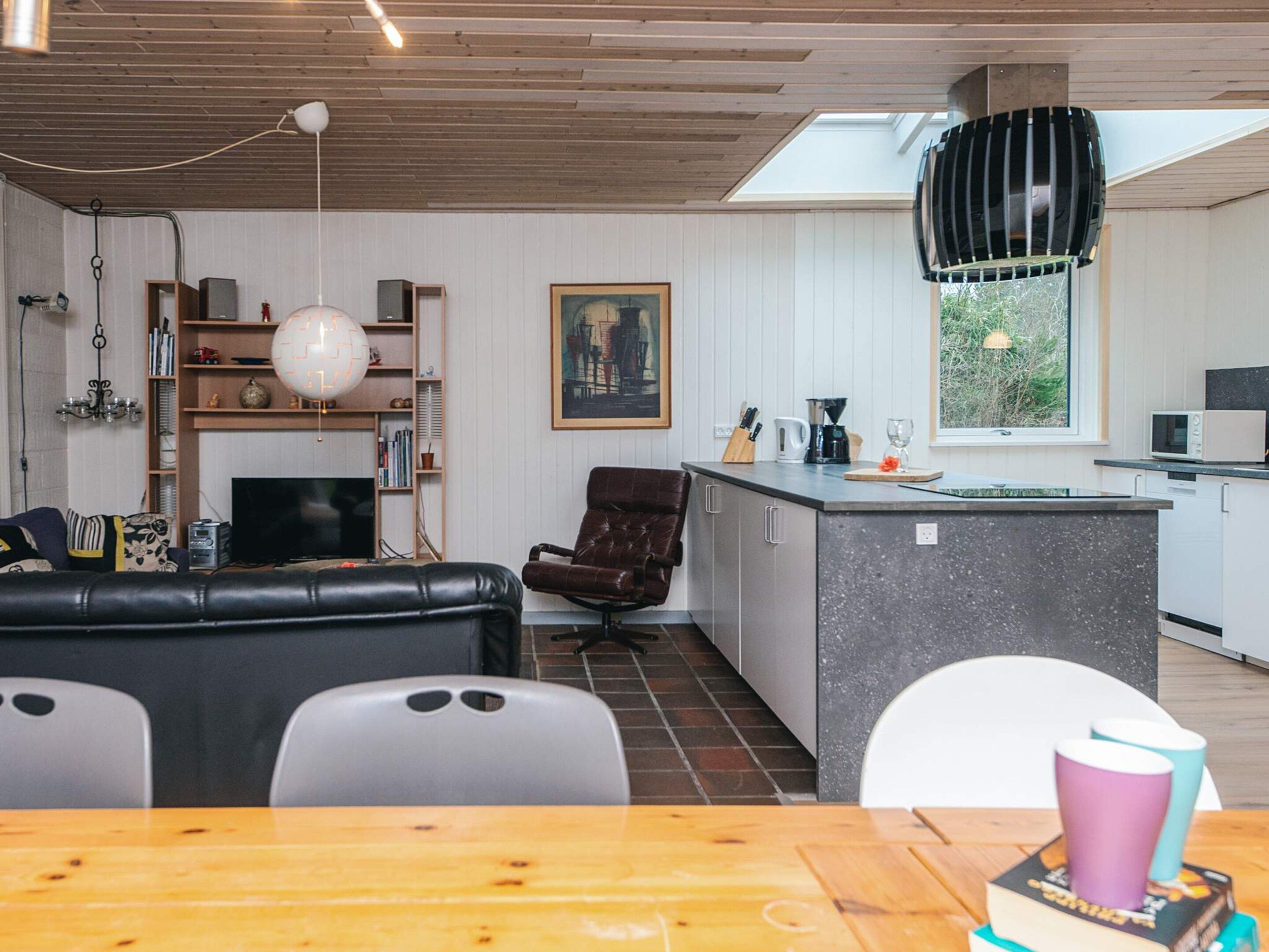 A modern kitchen with a central island, a dining area with a wooden table, and a living room with a sofa and chairs.