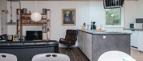 A modern kitchen with a central island, a dining area with a wooden table, and a living room with a sofa and chairs.