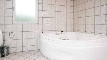 Une salle de bain avec une baignoire blanche, des toilettes et une fenêtre.