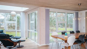 A modern interior with a wooden floor, large windows, and a dining area with chairs and a table.