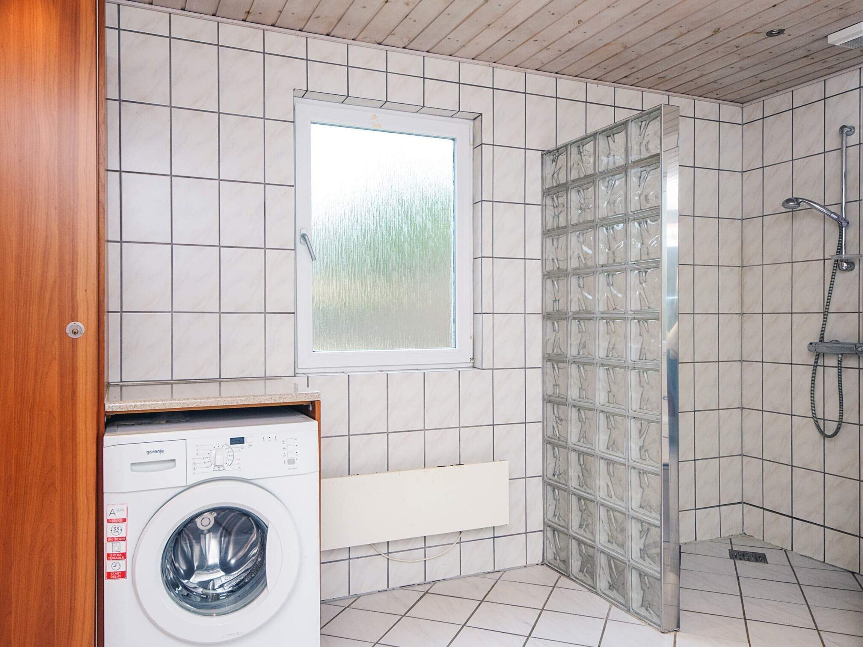 A compact bathroom with a washing machine, a shower enclosure, and a window.