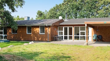 Une cabane en bois dotée d’un patio, de grandes fenêtres et d’un espace extérieur couvert aménagé en salon.