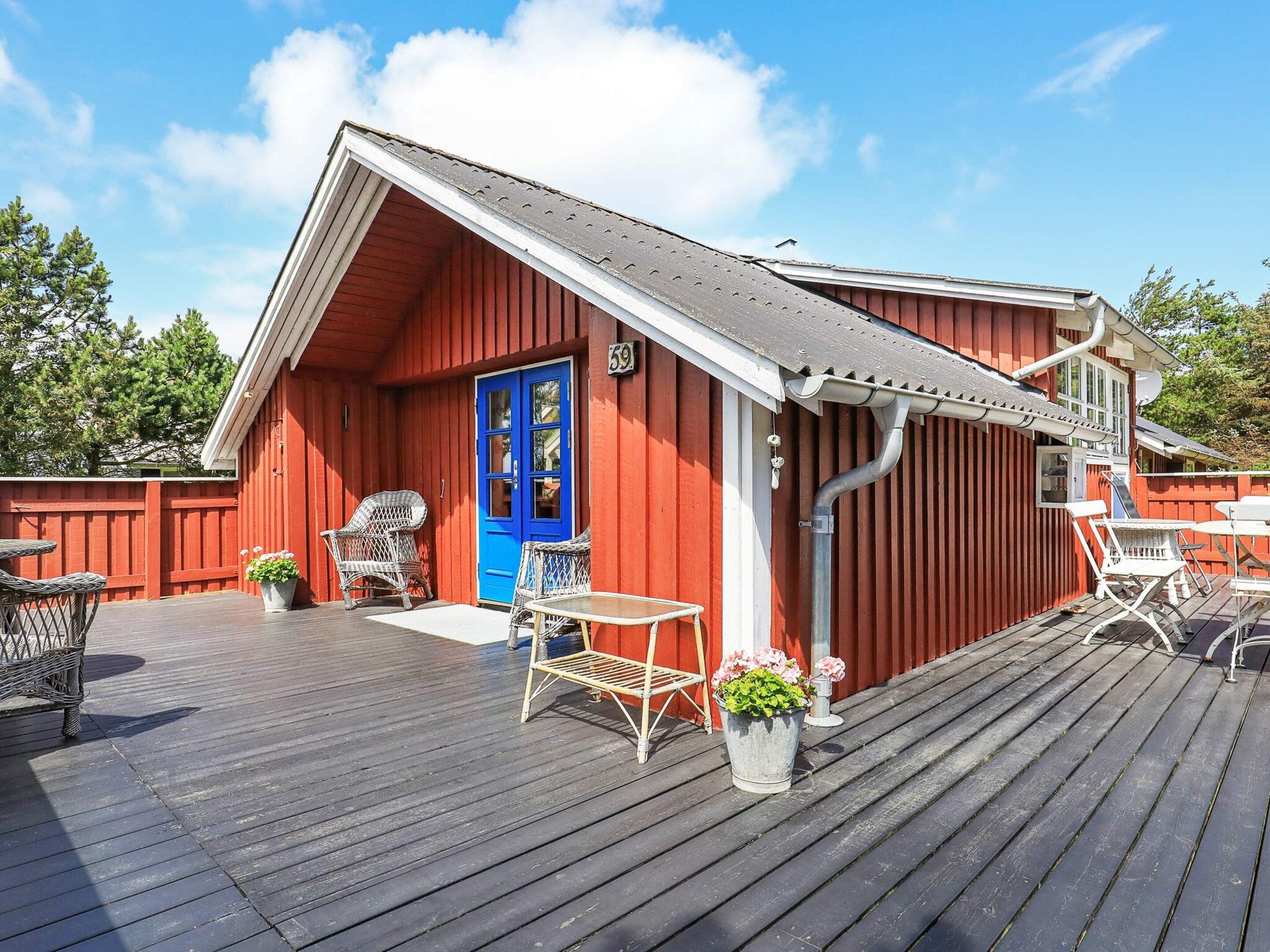 A red wooden building with a blue door, a covered deck with outdoor furniture, and a clear sky.