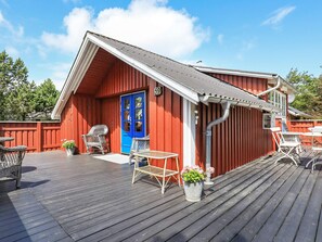 A red wooden building with a blue door, a covered deck with outdoor furniture, and a clear sky. - Holiday Home in Snedsted near Sea (Thisted)