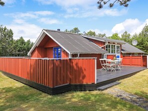 A red wooden building with a blue door, a deck, and a satellite dish. - Holiday Home in Snedsted near Sea (Thisted)
