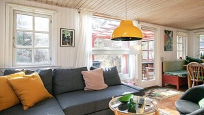 A cozy living room with a gray sofa, yellow pillows, a round glass coffee table, and a wooden chair. - Seaside Charm Near Blokhus Town-by Traum (Blokhus)