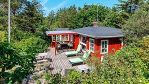A red cabin with a deck, surrounded by dense forest. - Seaside Charm Near Blokhus Town-by Traum (Blokhus)