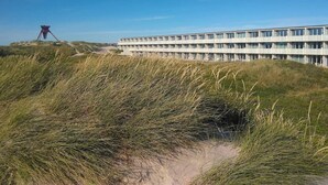 A modern building with a flat roof and multiple windows, surrounded by grassy dunes. - Seaside Charm Near Blokhus Town-by Traum (Blokhus)