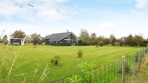 A large, open grassy yard with a fenced area, a house with a sloped roof, and a small shed in the background. - 6 Person Holiday Home in Humble (Sydlangeland)