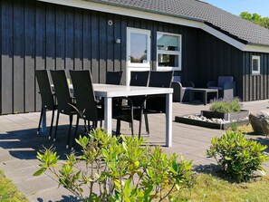 A patio with a table and chairs, a small garden area, and a building with a dark exterior and a sloped roof. - 6 Person Holiday Home in Humble (Sydlangeland)