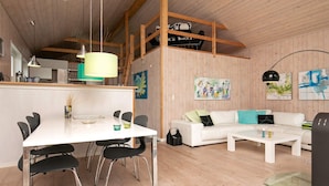 A modern living room with a white sofa, a dining table with chairs, and a kitchen area with wooden beams. - 6 Person Holiday Home in Humble (Sydlangeland)