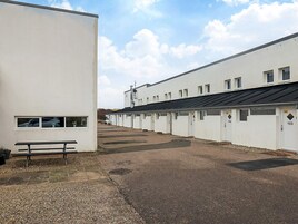 A row of white, single-story buildings with numbered doors, a gravel parking area, and a bench.