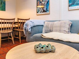 Una habitación con un sofá azul, una mesa de madera y una silla. Hay jarrones decorativos sobre la mesa.