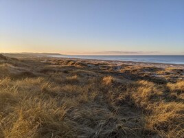 A coastal landscape with grassy dunes and a clear view of the sea.