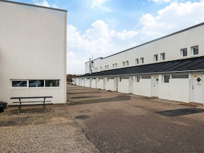 A row of white buildings with numbered doors, a gravel path, and a bench. - 6 Person Holiday Home in Brovst (Brovst)