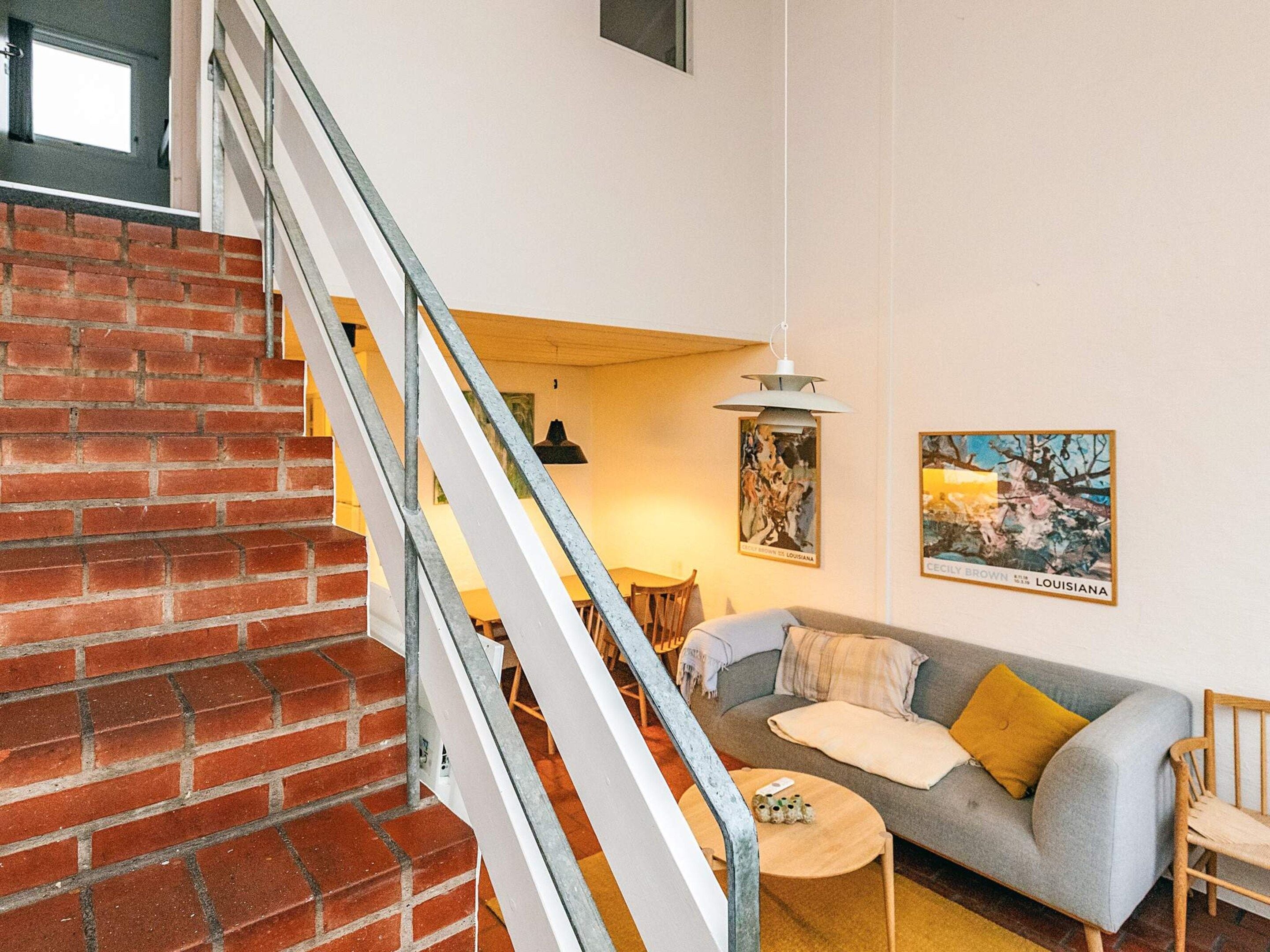 A staircase with a brick wall, a gray sofa with cushions, a small round table, and two wall-mounted pictures.