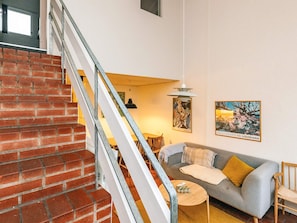 A staircase with a brick wall, a gray sofa with cushions, a small round table, and two wall-mounted pictures. - 6 Person Holiday Home in Brovst (Brovst)