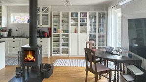 A modern kitchen with a wood-burning stove, white cabinetry, and a dining area with a table and chairs. - Holiday Home in Henån (Henån)