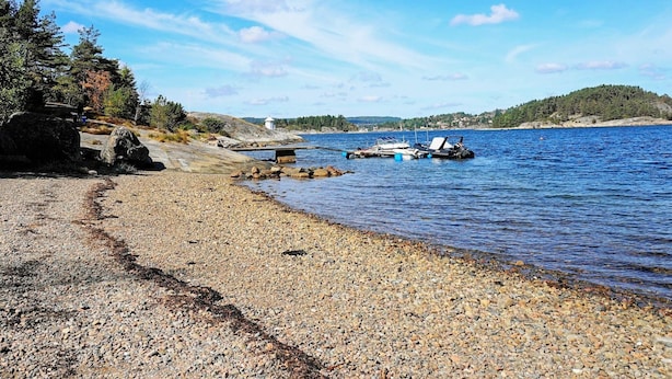 A pebbly beach with boats, a lighthouse, and a forested hill in the background. - Holiday Home in Henån (Henån)