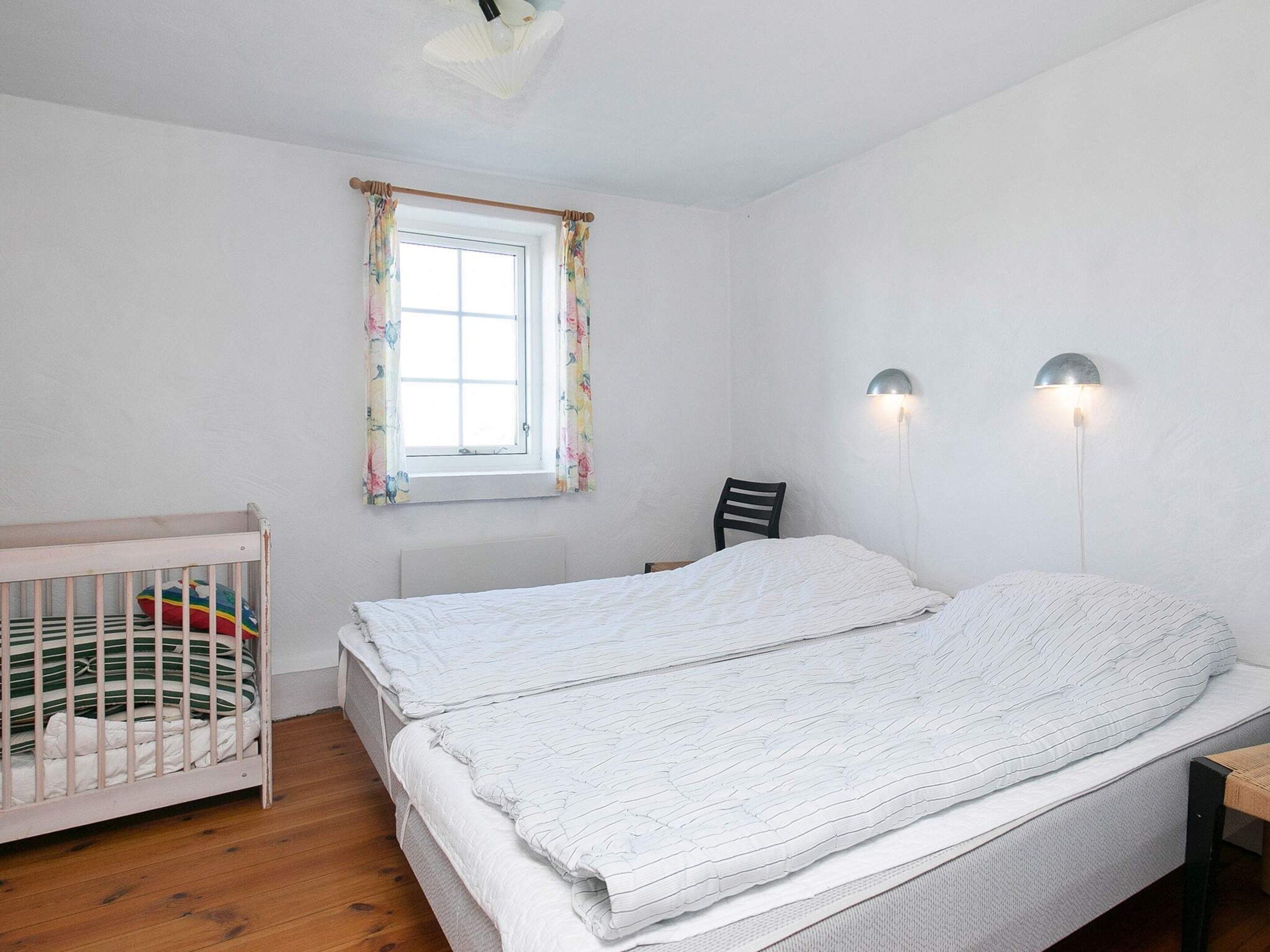 Quarto com berço, cama, janela com cortinas e duas luminárias fixadas na parede.
