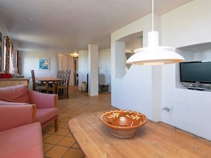 A living room with a sofa, a wooden table, a bowl, a TV, and a dining area in the background.