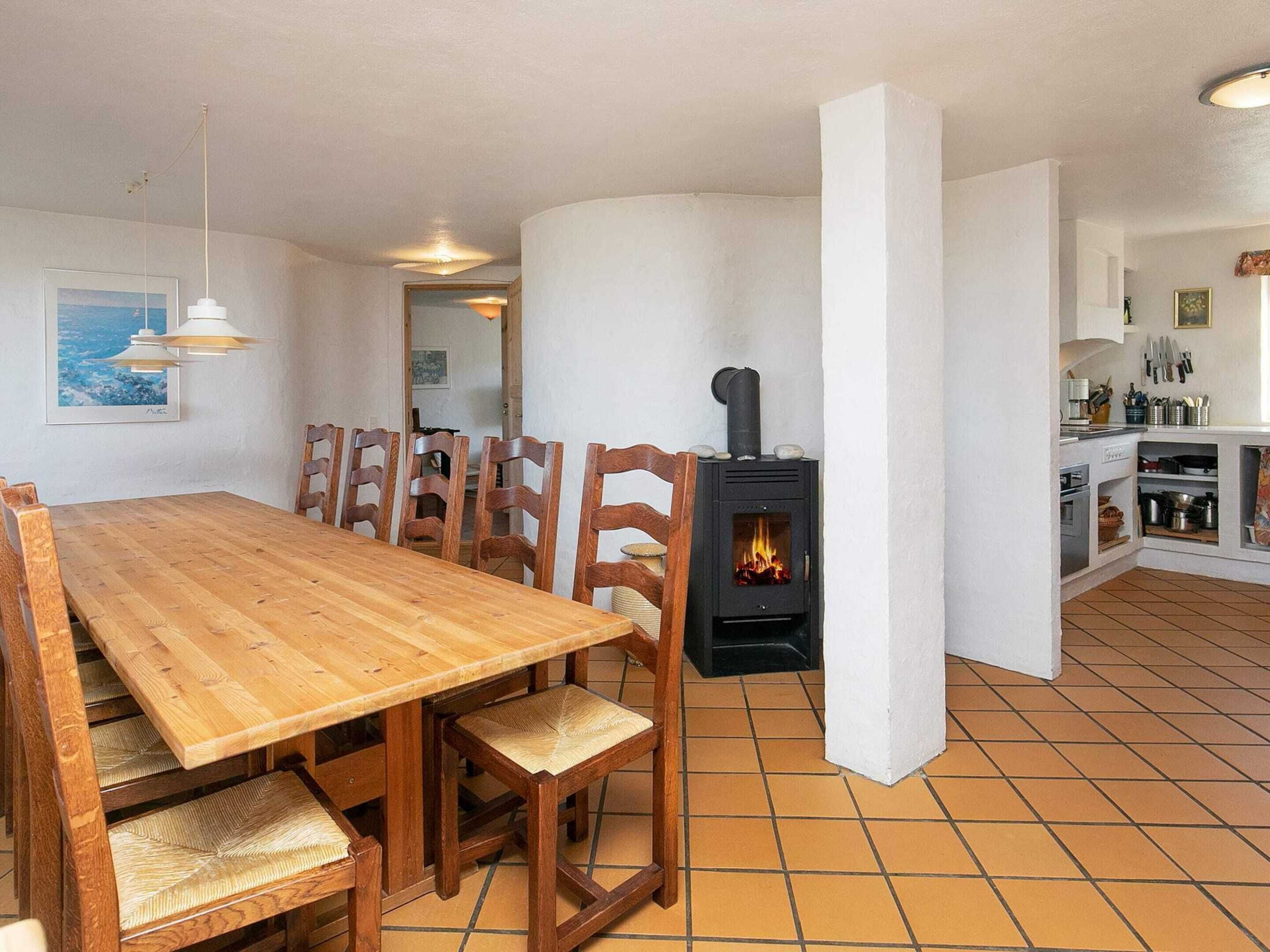 A dining area with a wooden table and chairs, a built-in wood stove, and a kitchen with cabinets and utensils.