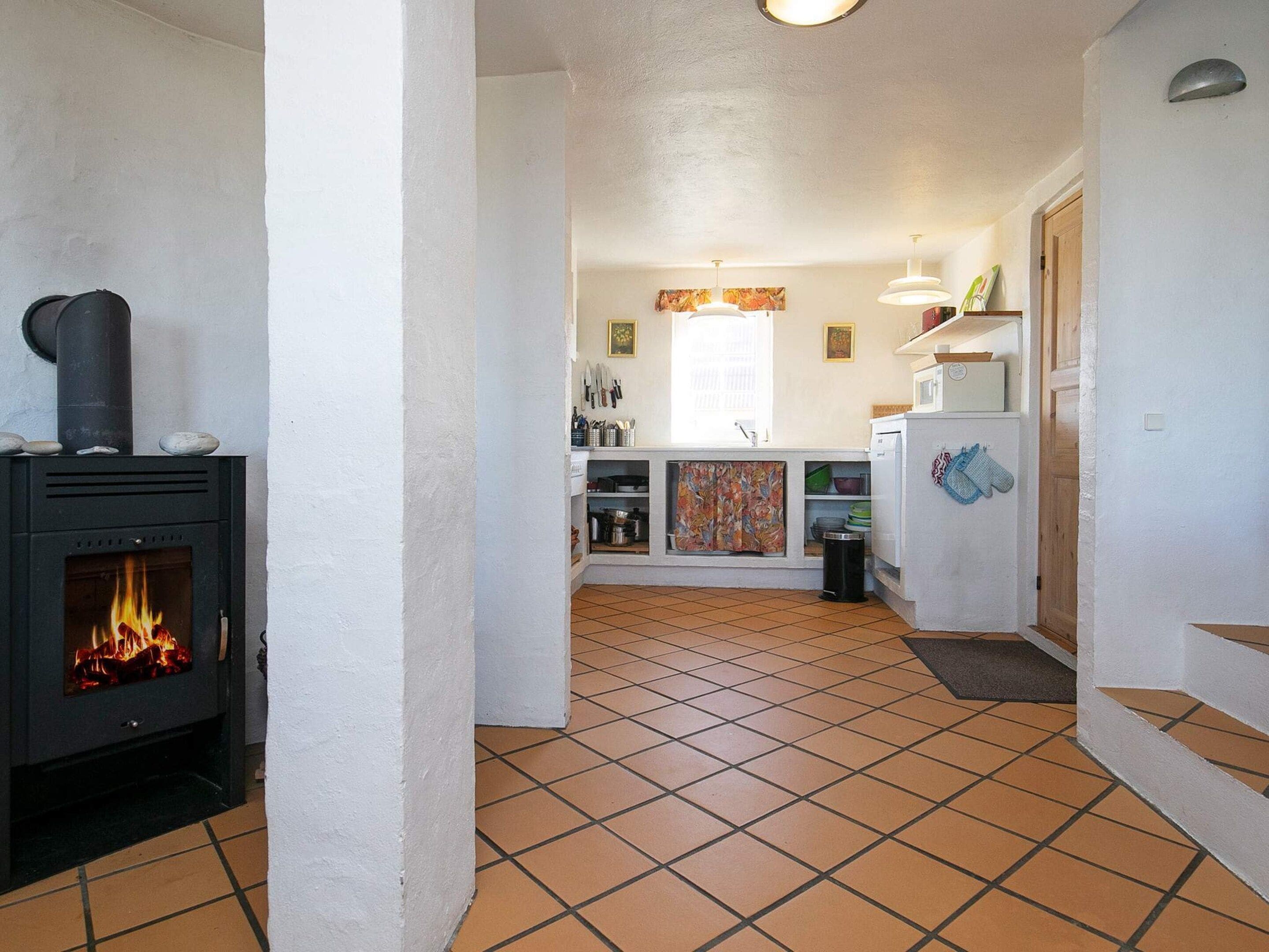 Uma cozinha com piso ladrilhado, fogão com chama visível e janela com cortinas.