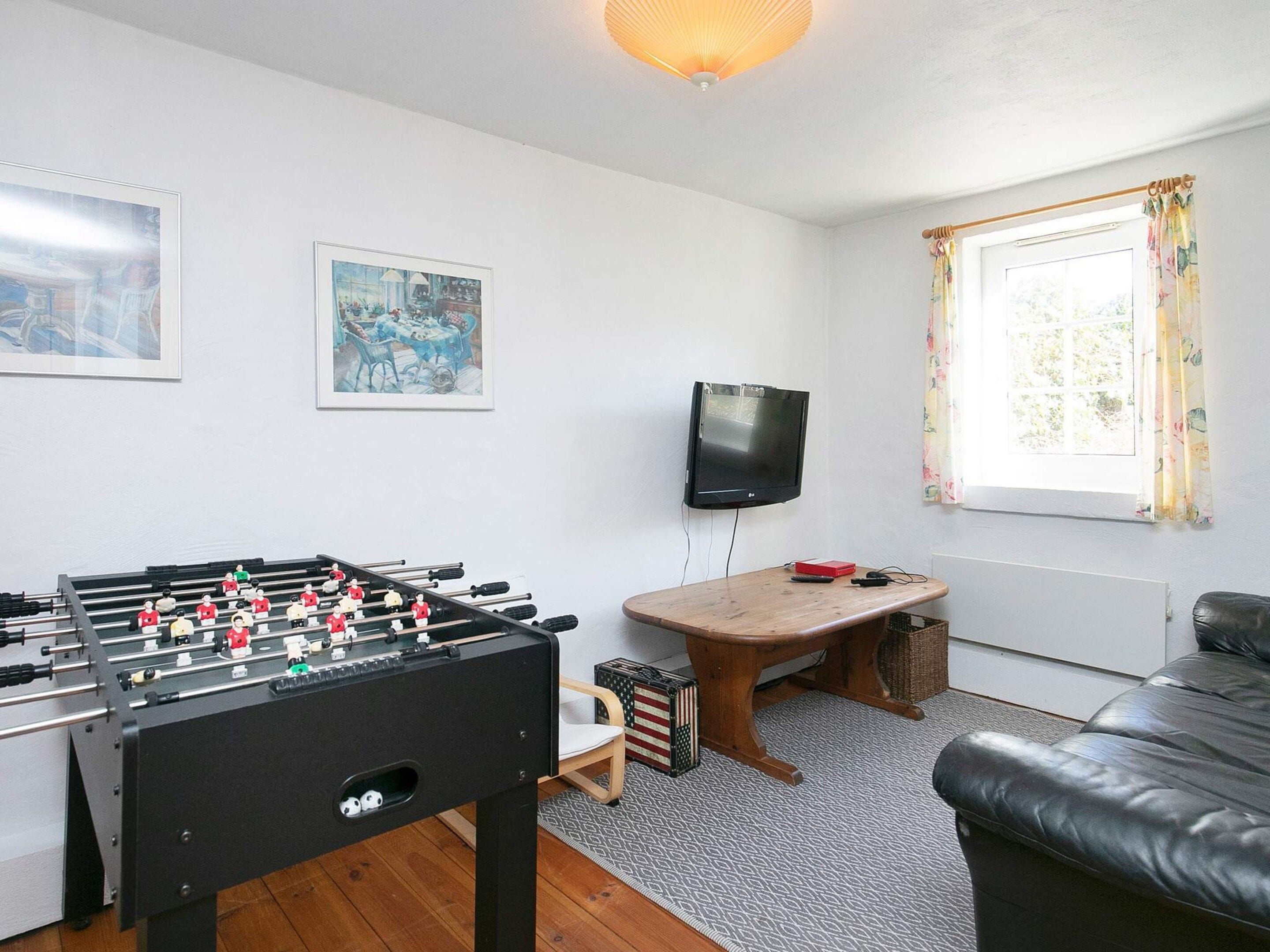 Quarto com mesa de futebol, televisão, janela com cortinas e sofá.