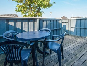 An outdoor patio with a round table and four chairs, surrounded by a wooden deck and a wooden fence. - Holiday Home in GrenÃ¥ near Sea (Grenaa)