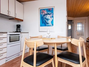 A kitchen with a white stove, wooden cabinets, a coffee maker, and a framed abstract painting on the wall. - Holiday Home in GrenÃ¥ near Sea (Grenaa)