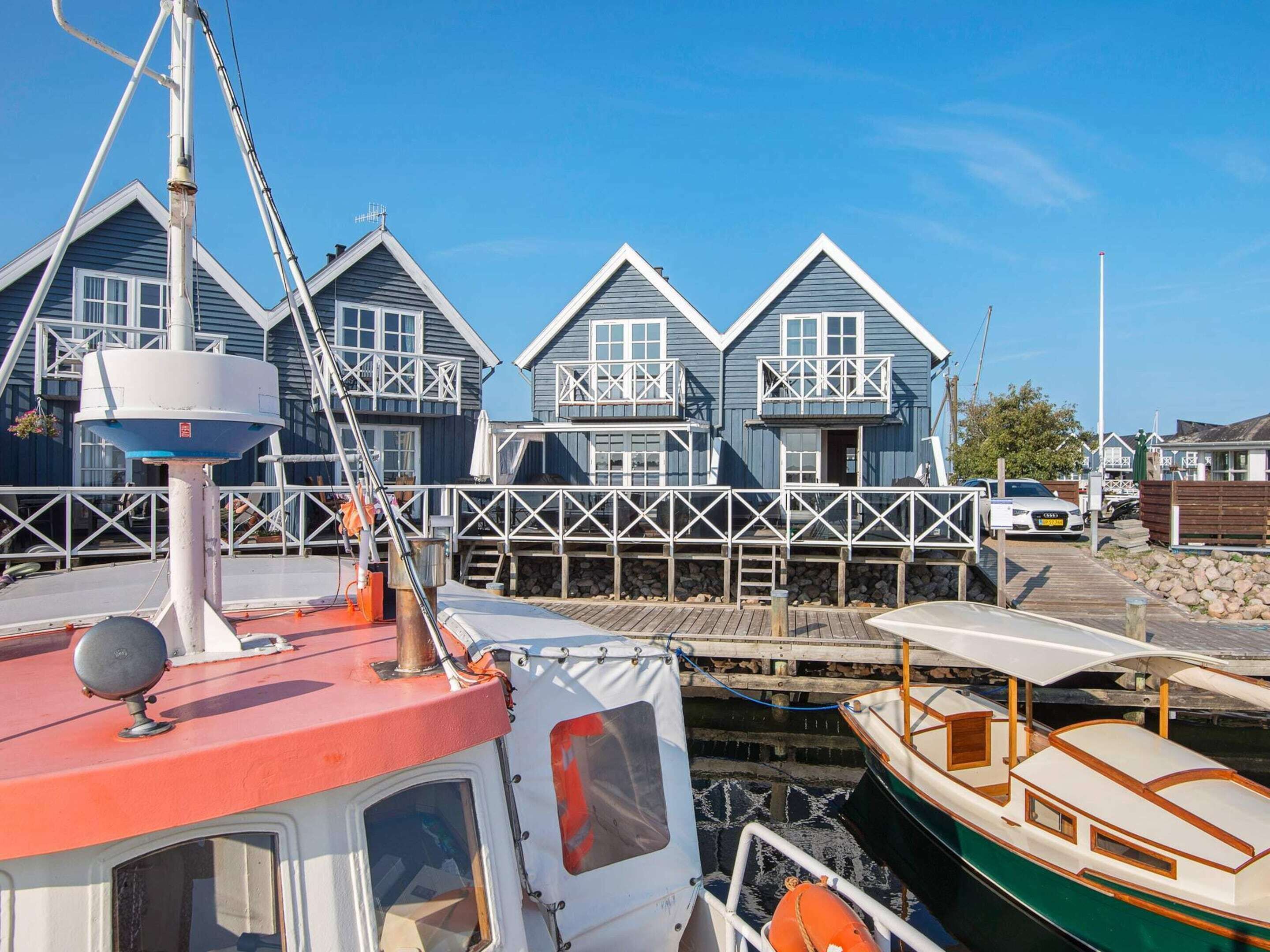 A docked boat with a cabin and a white superstructure, a pier leading to a row of blue houses with white railings, and a clear blue sky.