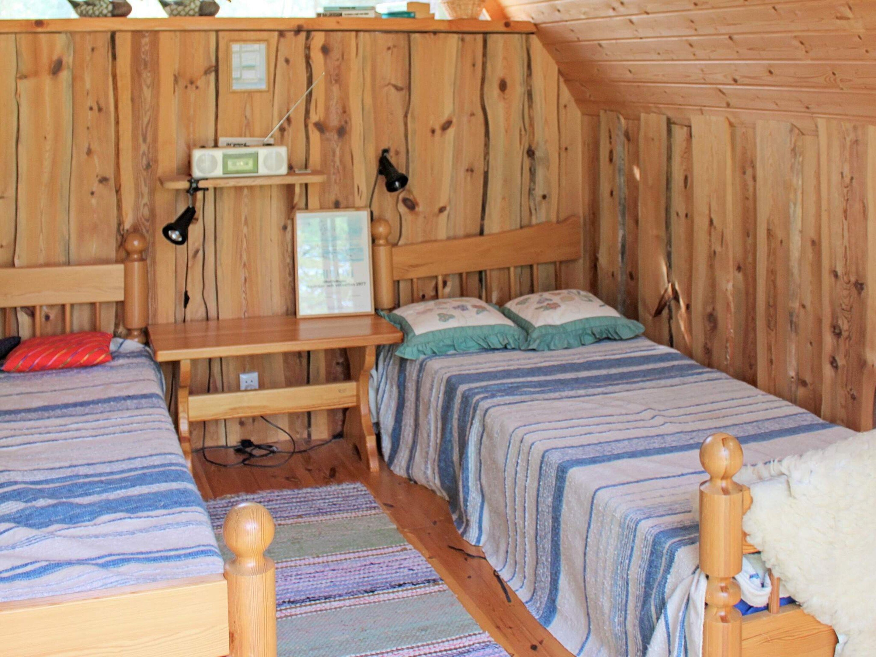 A wooden cabin room with two beds, a desk, and a radio.