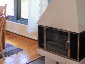 A room with a fireplace, a window with curtains, a radiator, and a wooden floor.