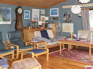 A room with a wooden floor, a sofa, two armchairs, a table, and various wall decorations including paintings and a clock. - 6 Person Holiday Home in Lidkoping (Lidköping)