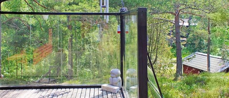 A wooden deck with a glass enclosure overlooking a forested area.