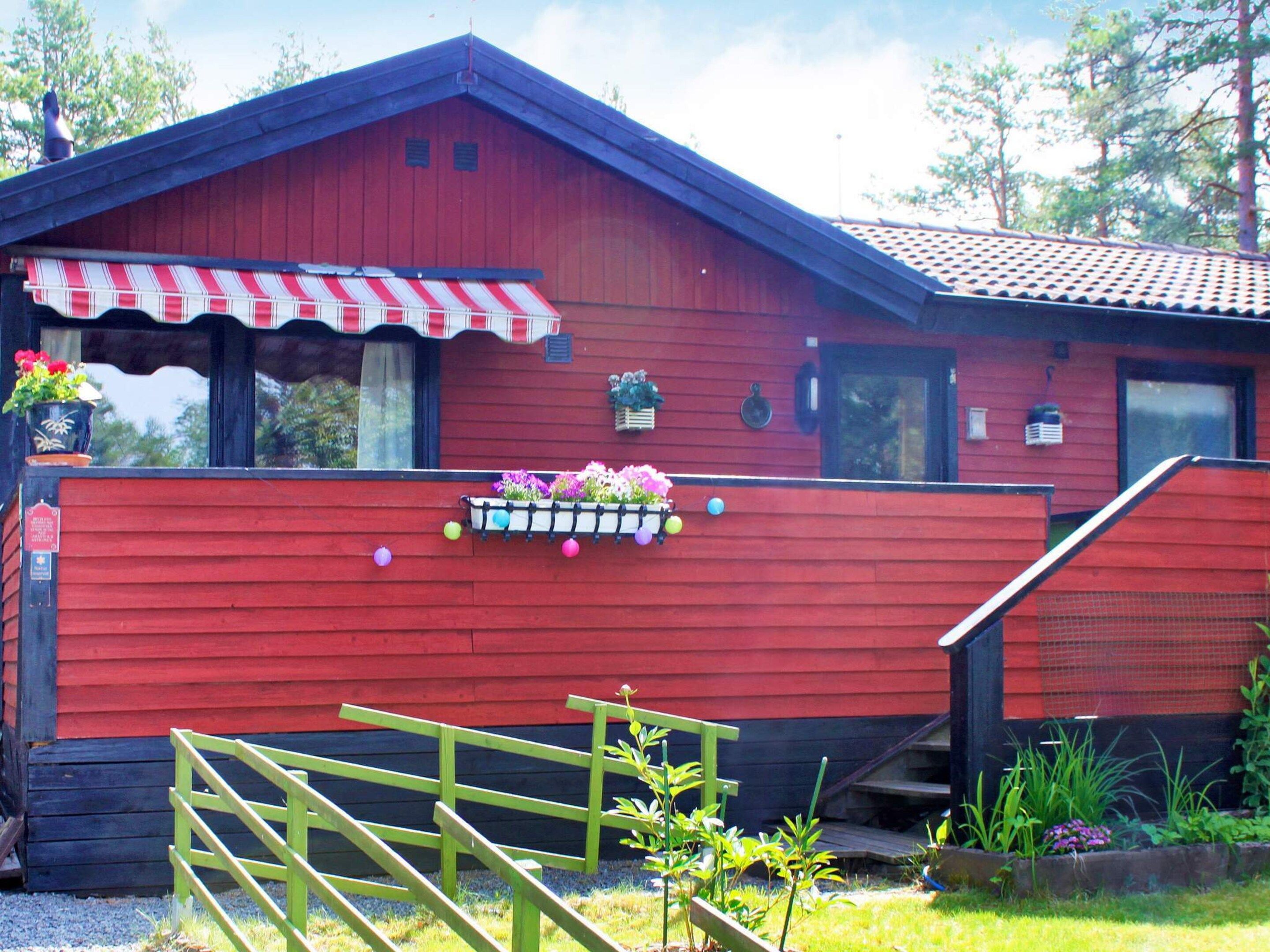 A red wooden building with a red and white striped awning, a flower box on the front, and a wooden fence in front.